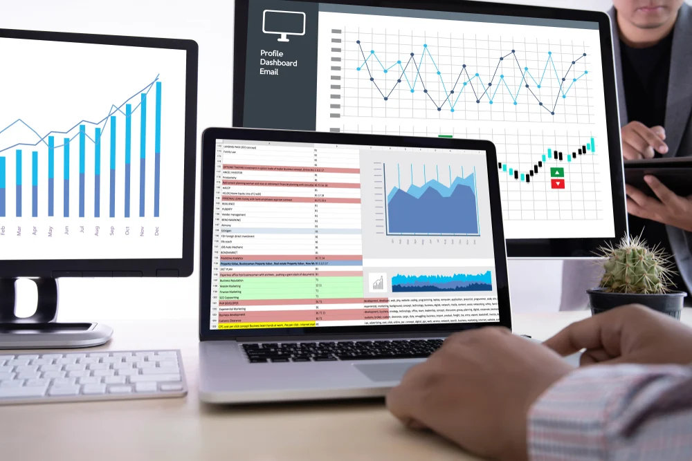 Photograph of three laptop monitors with various graphs and google analytics reports