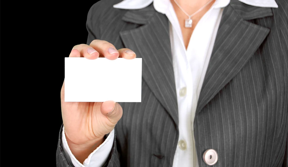 A person in a suit holding a plain white business card.