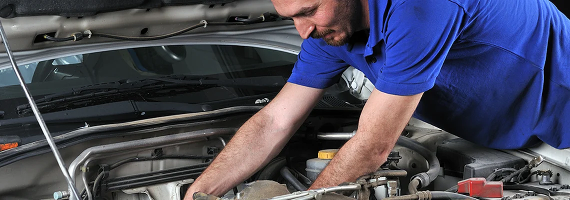 A car mechanic wearing a blue polo while working on fixing the engine to a car.