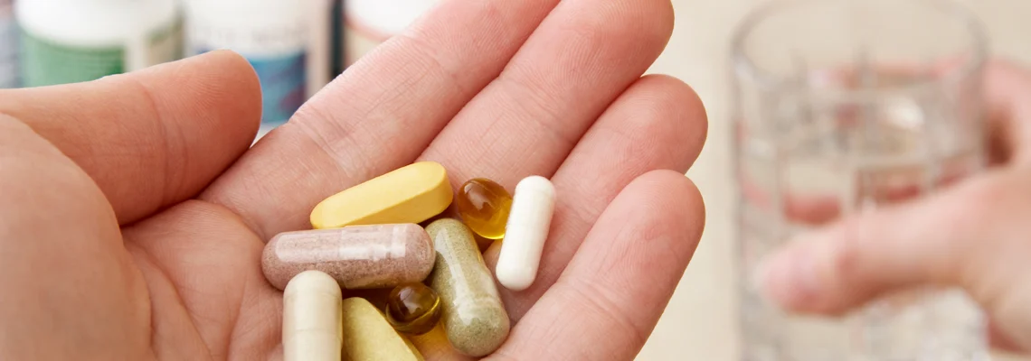 A person holding various pills in their hand with a glass of water too.