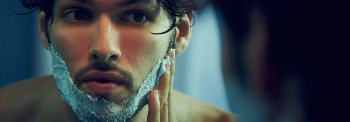 A person placing shaving foam on their beard, preparing to shave.