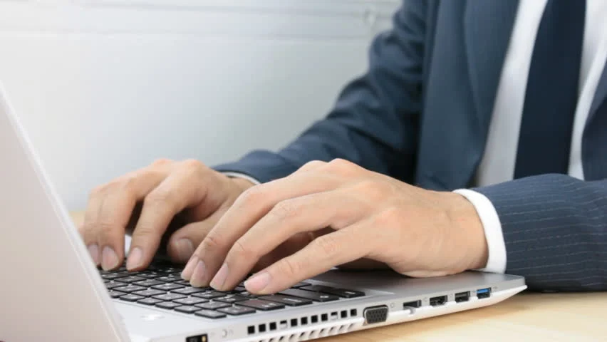 A person in a suit typing on their laptop.