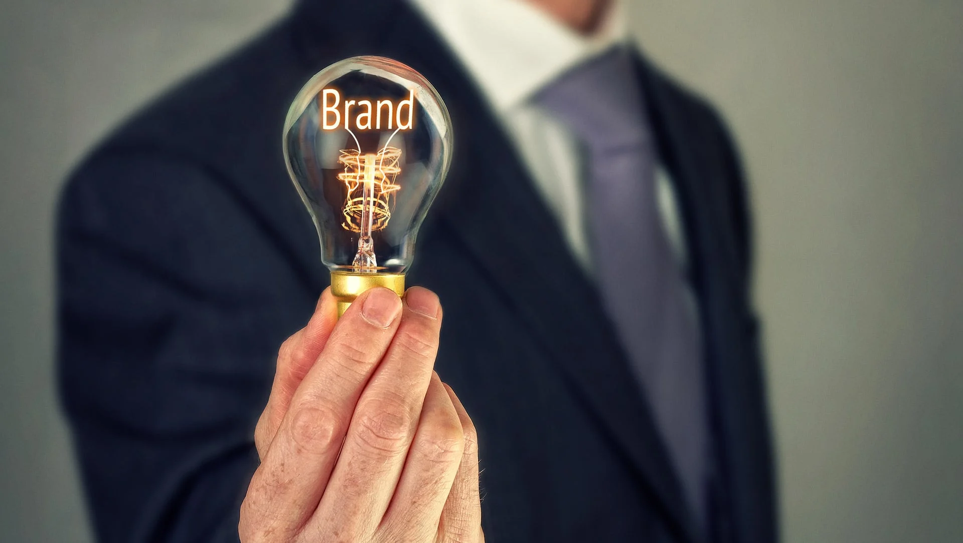 A person in a white shirt, blue tie and black blazer holding a lightbulb with "brand" text inside the bulb.