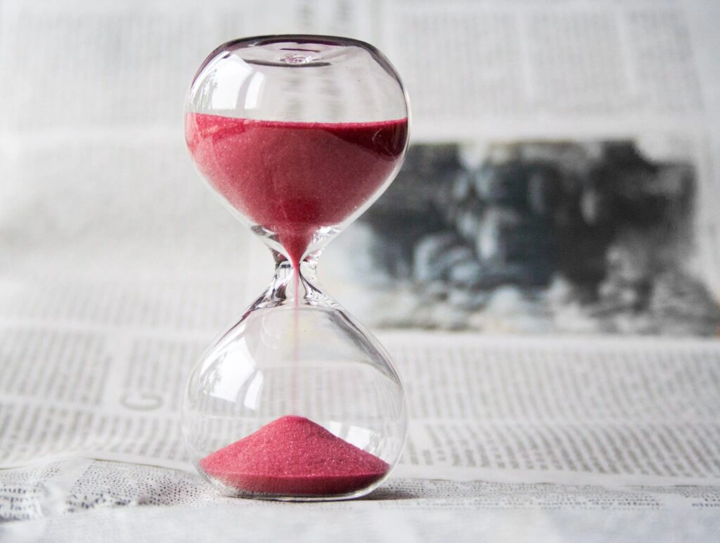 Hourglass with red sand running, resting on a newspaper Hourglass with red sand running, resting on a newspaper