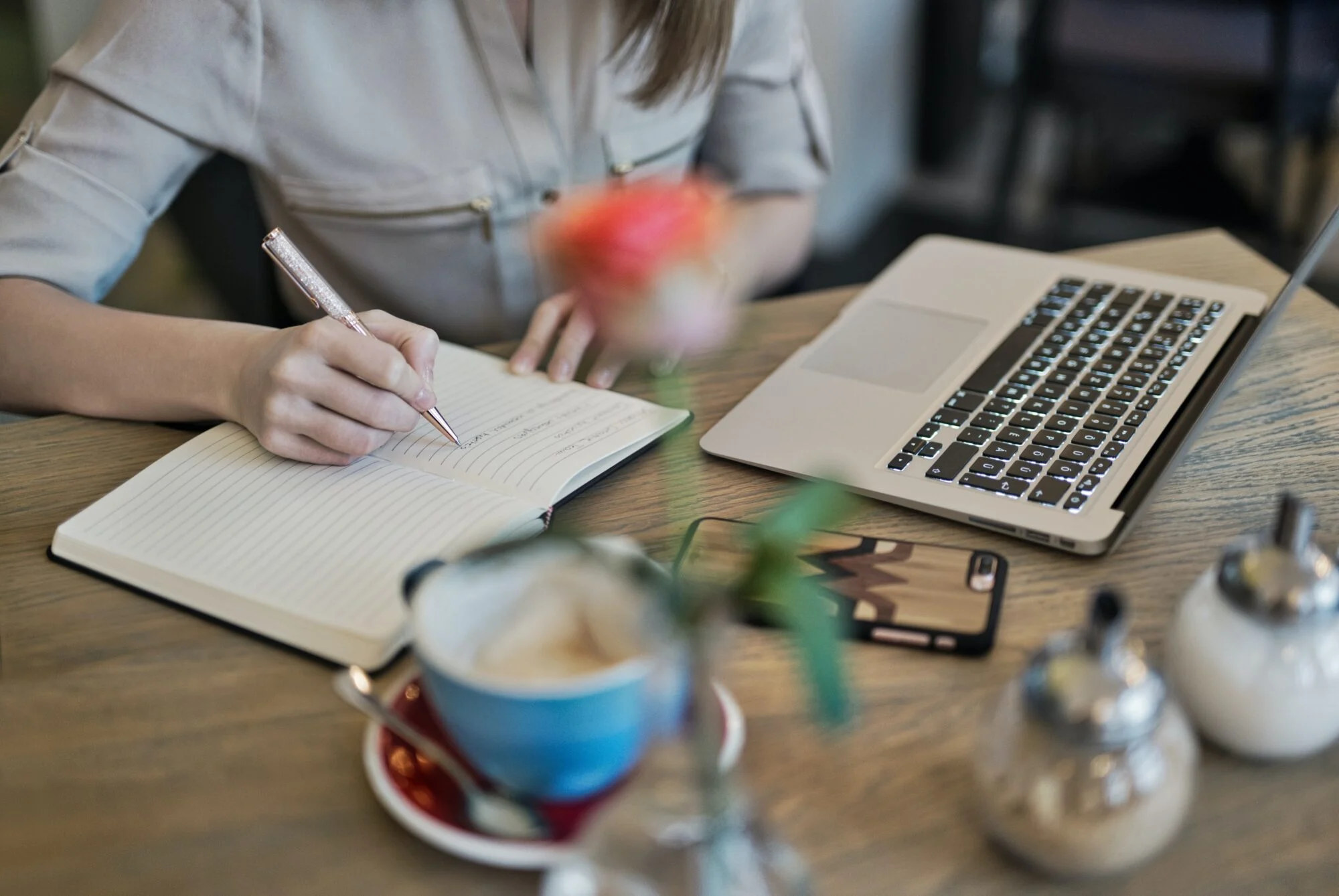 Woman writing notes in a notebook beside a laptop and coffee