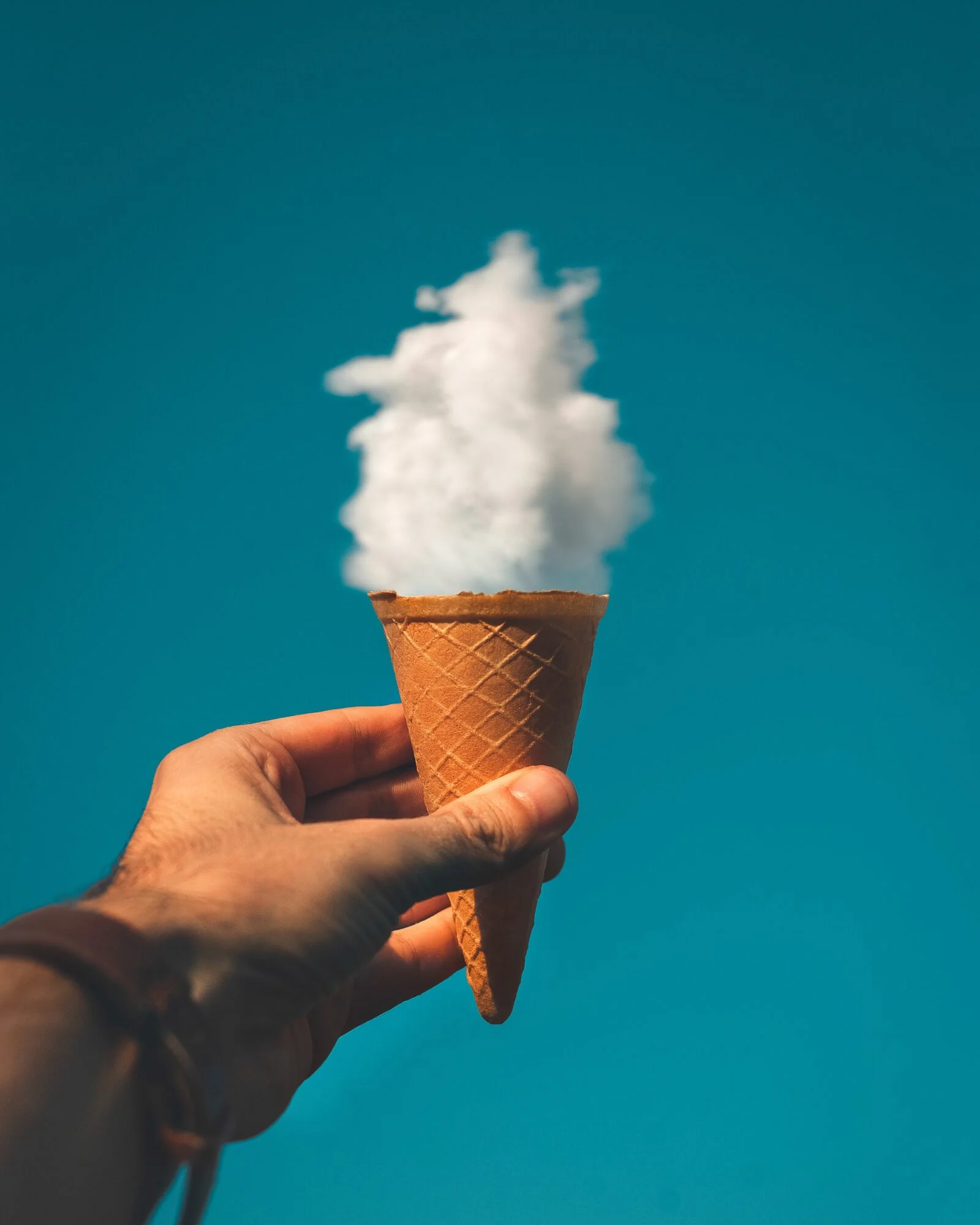 An ice cream cone being held up in the sky to make a cloud look like the ice cream.