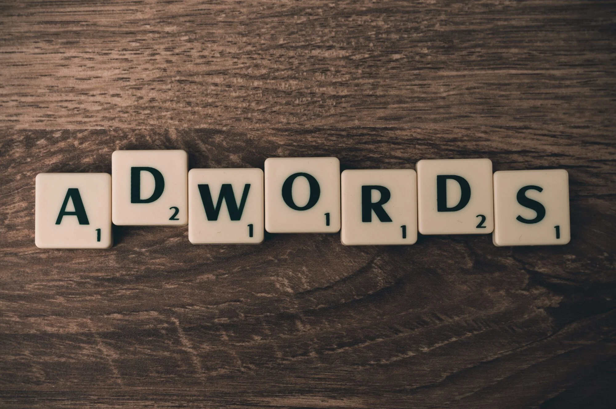 A selection of scrabble letters on a wooden table spelling the word Adwords.