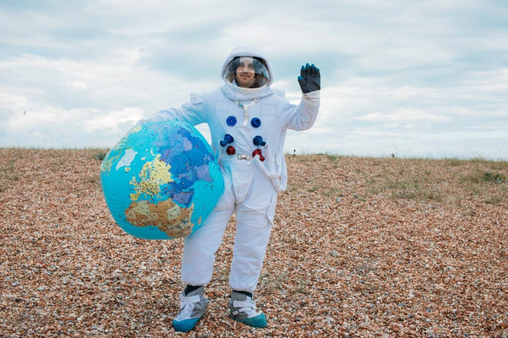 Person in an astronaut costume waving while holding an inflatable globe