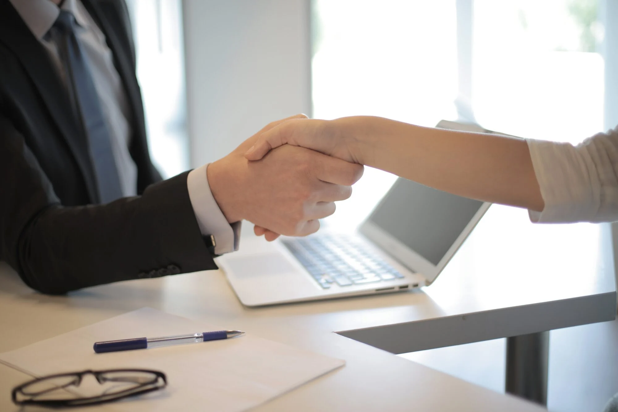 Business handshake across a desk with a laptop in the background