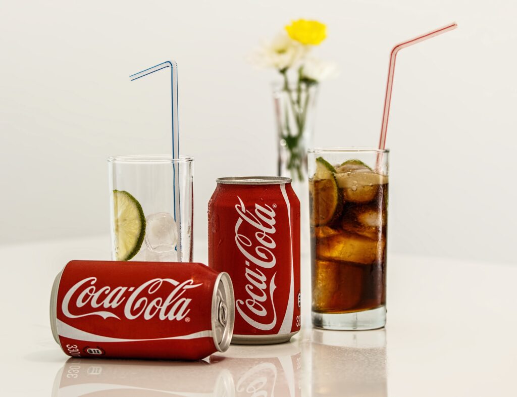 Two cans of CocaCola with a glass.