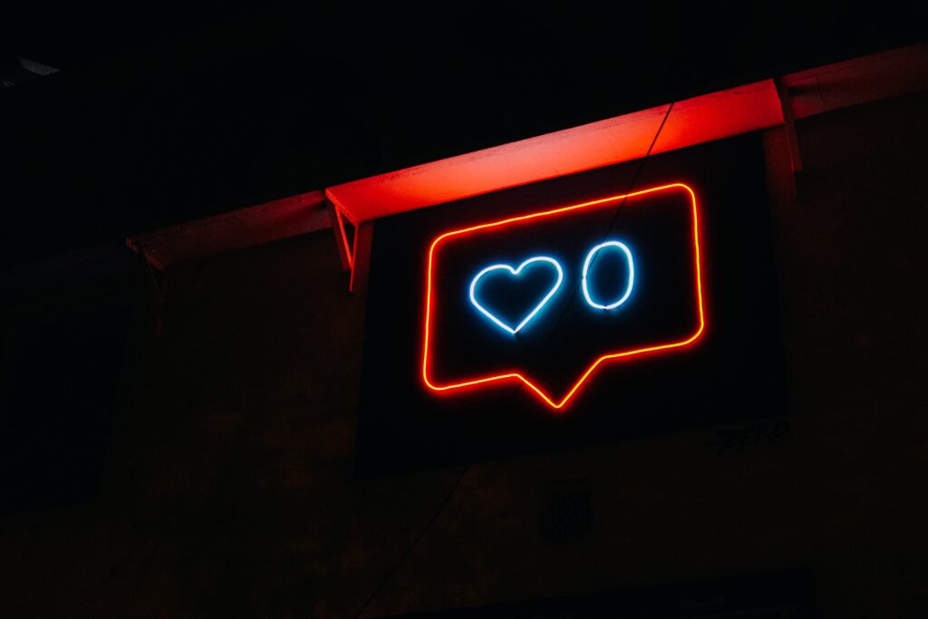A dark room with a neon instagram like sign displaying zero likes.