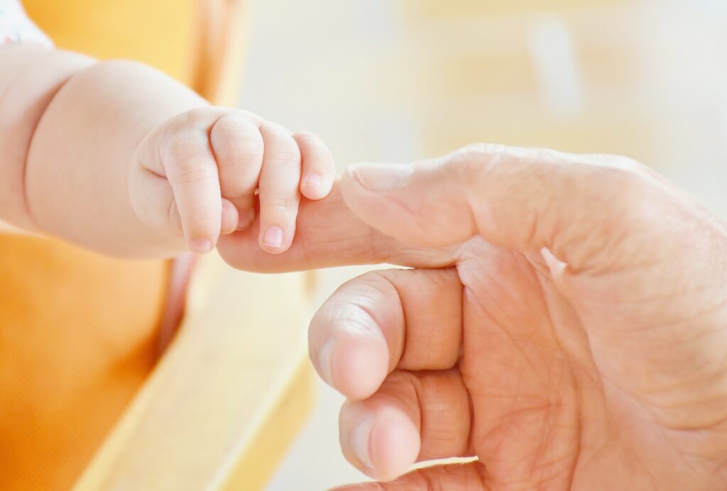 A baby's hand holding the finger of a parent. 