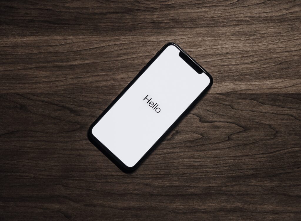 An iPhone on a wooden desk that is rebooting with the "hello" text appearing over a white background. 