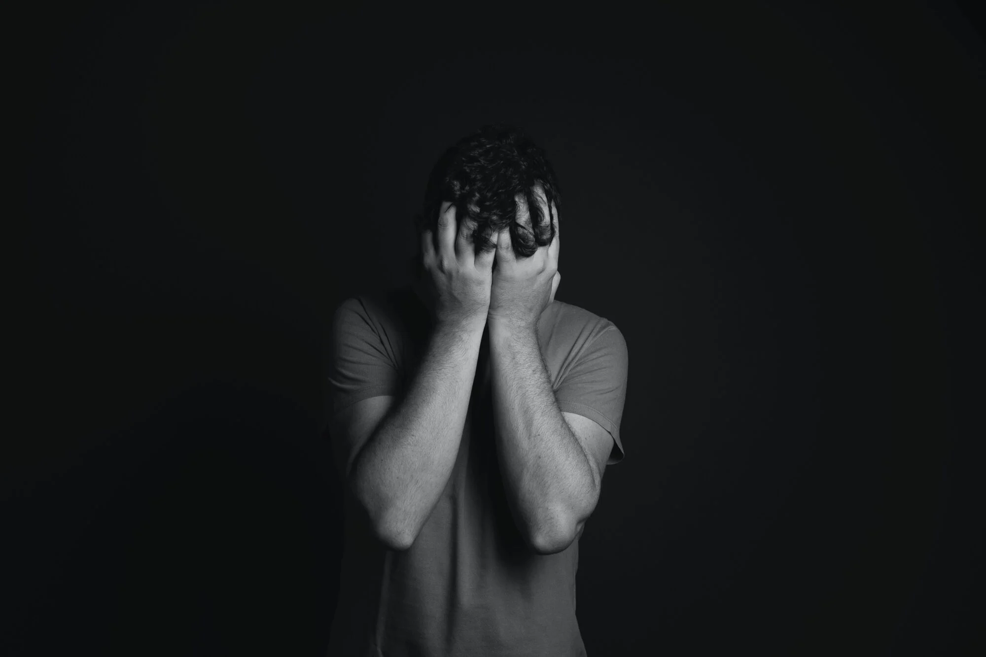 A black and white image of a man looking upset with his head in his hands.