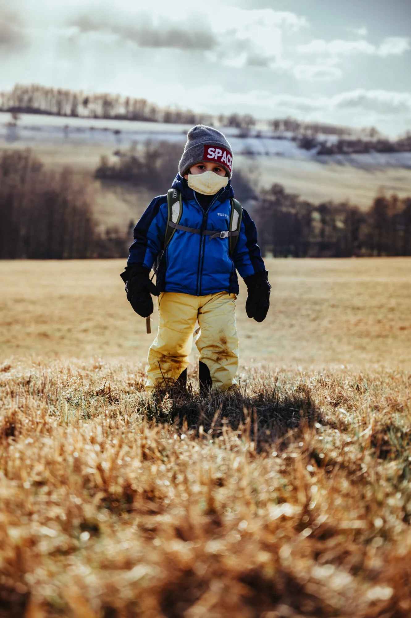 A child on a hike wearing a blue coat and a facemask