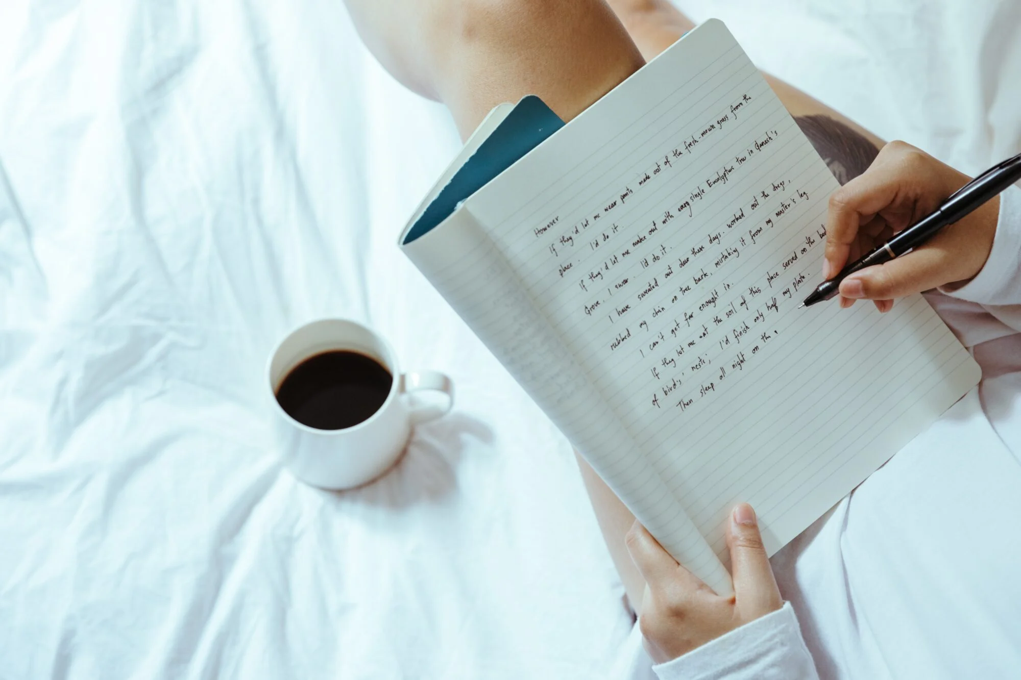 A person whiting on a notepad with a cup of coffee beside them.