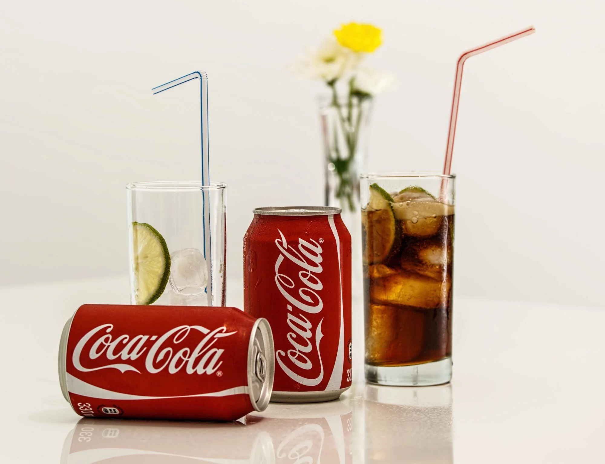 Two cans of CocaCola with a glass.