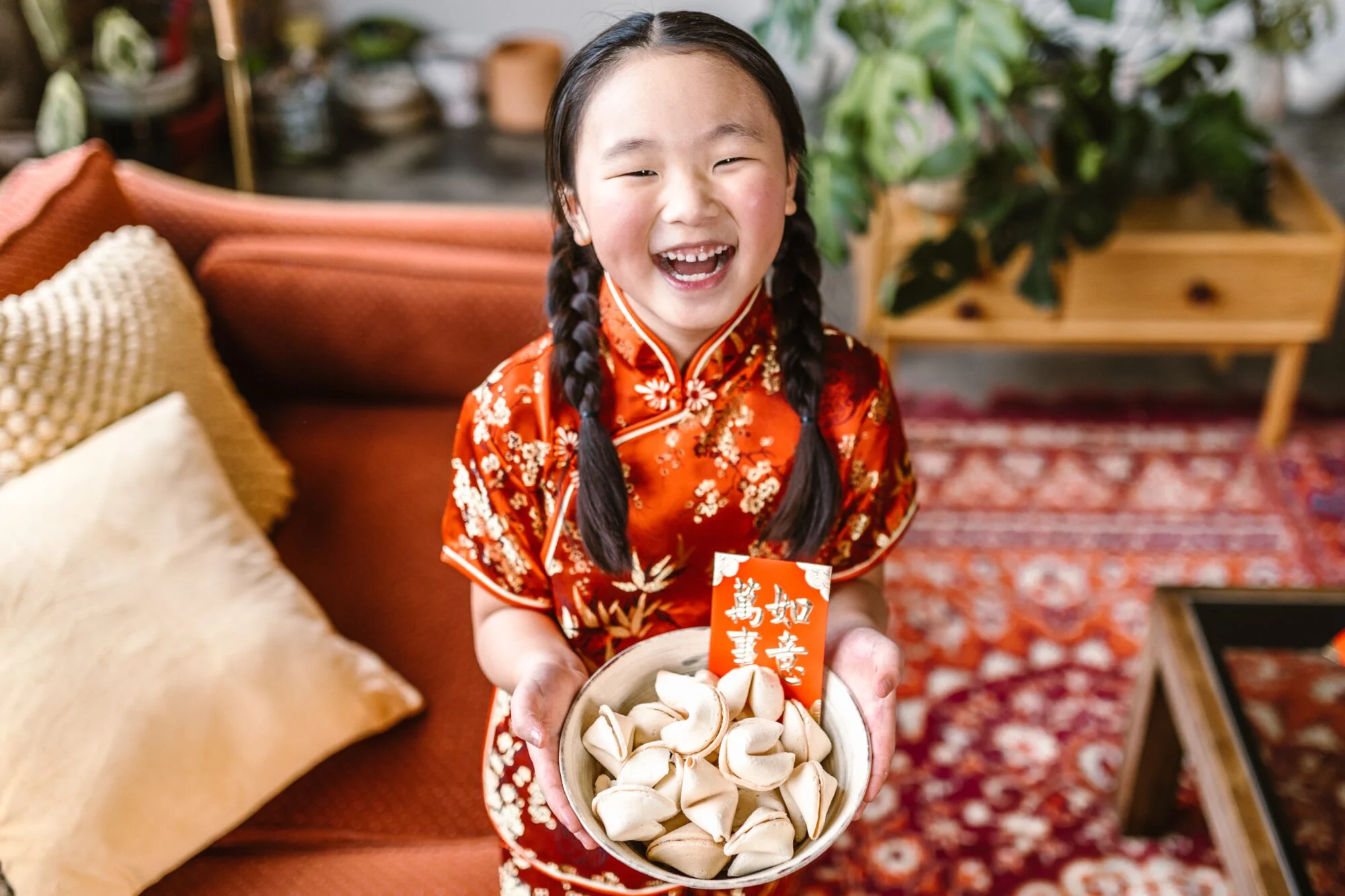 Smiling girl in a red dress holding a bowl of fortune cookies and a red envelope for Chinese New Year Smiling girl in a red dress holding a bowl of fortune cookies and a red envelope for Chinese New Year