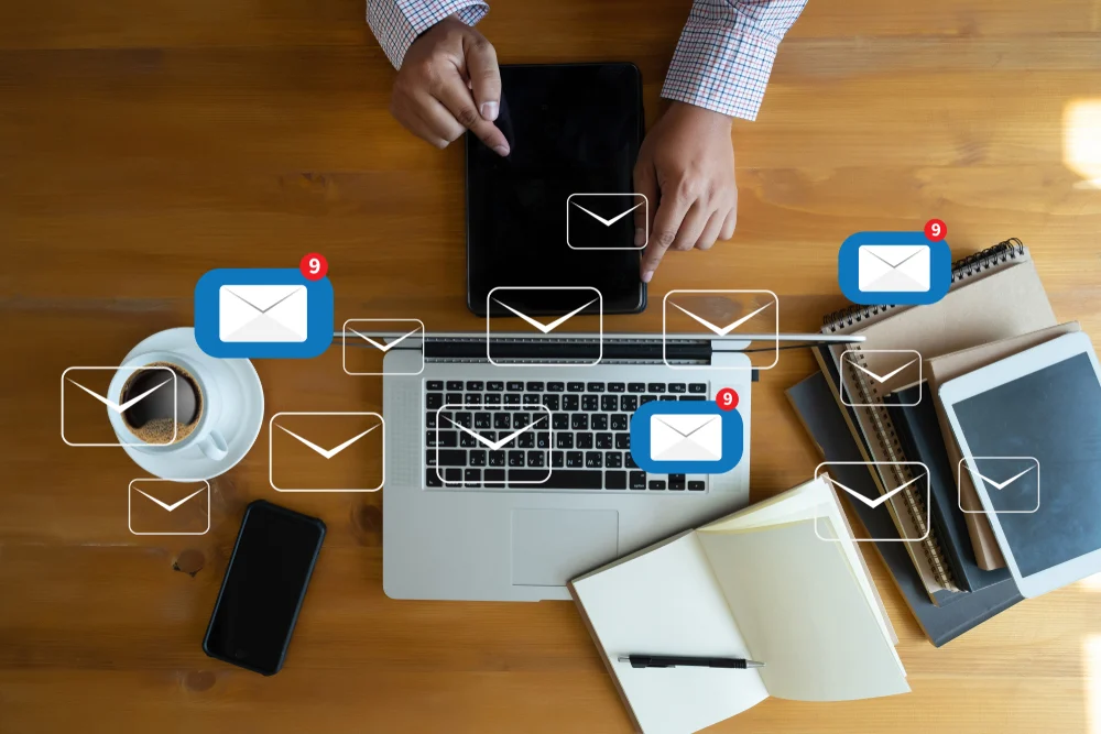 Birdseye photograph of an email apprentice sat at a wooden desk with his laptop and notebook with email icons overlaid on the image