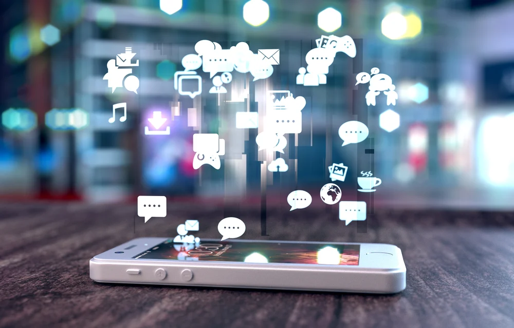 White smart phone on a wooden table emitting holographic image of social media related icons