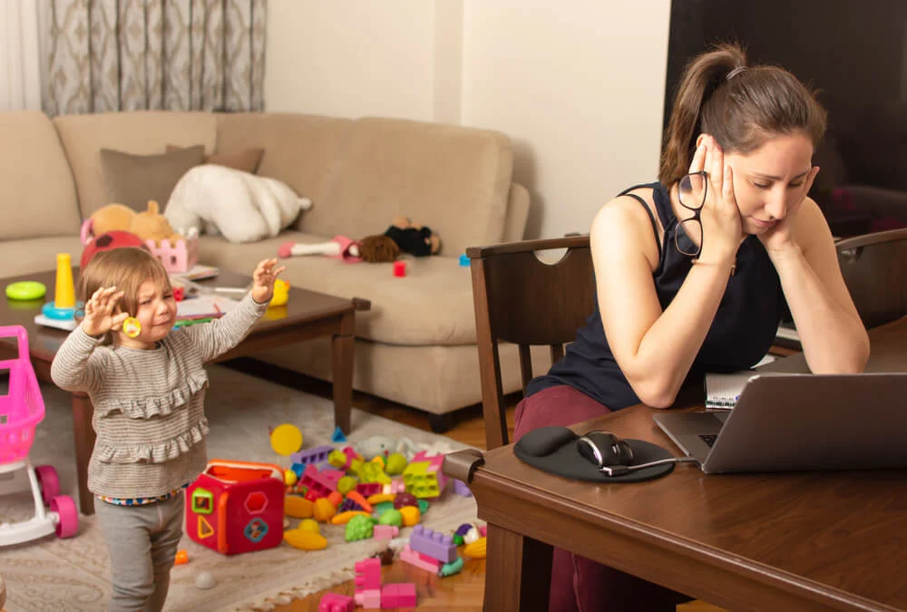 Tired mother trying to work on a laptop at home whilst her child is crying.