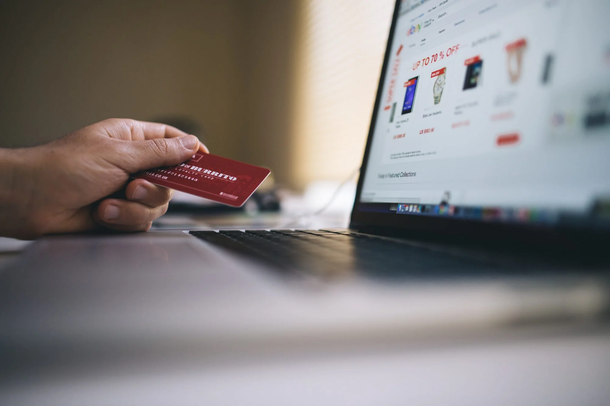A person holding their credit card while shopping on an e-commerce store on their laptop. 