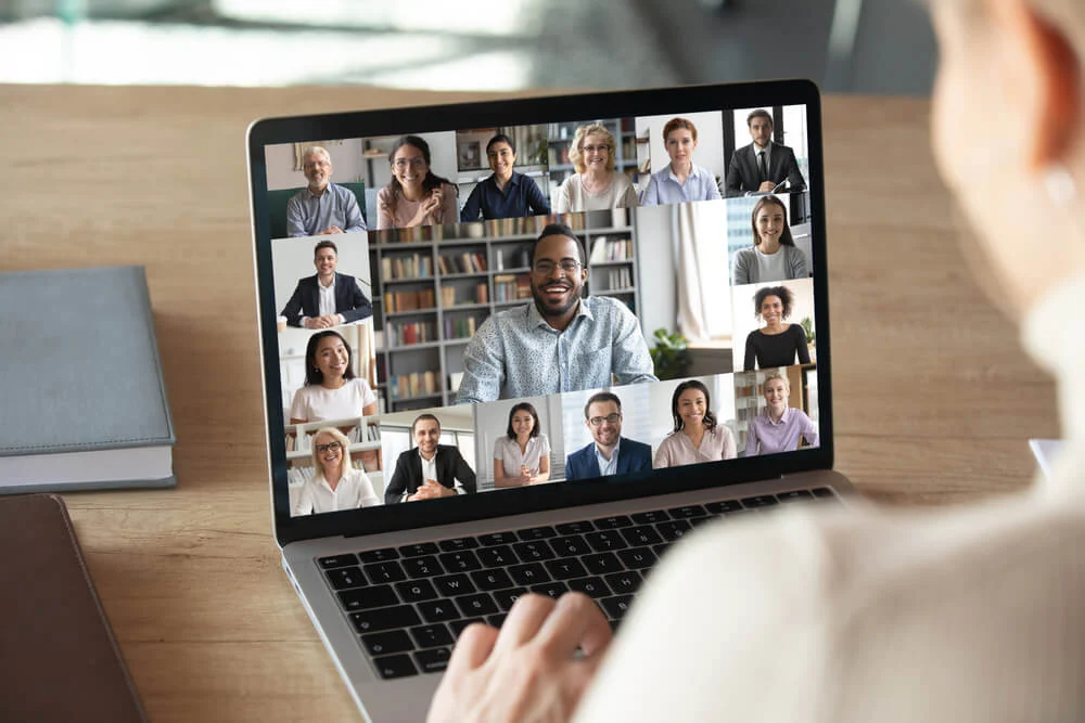 Back view of female employee on a video call with multiple colleagues on a modern laptop at home