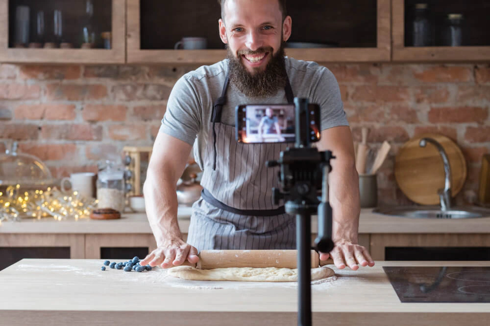 Man filming himself rolling dough with a smartphone mounted on a tripod Man filming himself rolling dough with a smartphone mounted on a tripod