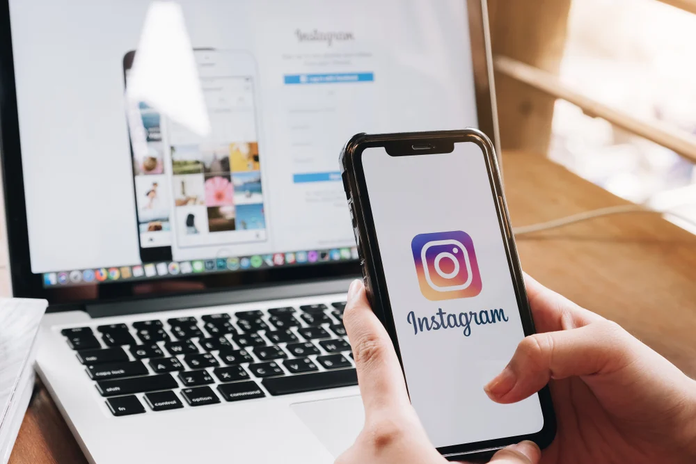 A person opening Instagram on their MacBook laptop and iPhone ready to share posts after learning how to take good Instagram photos. 
