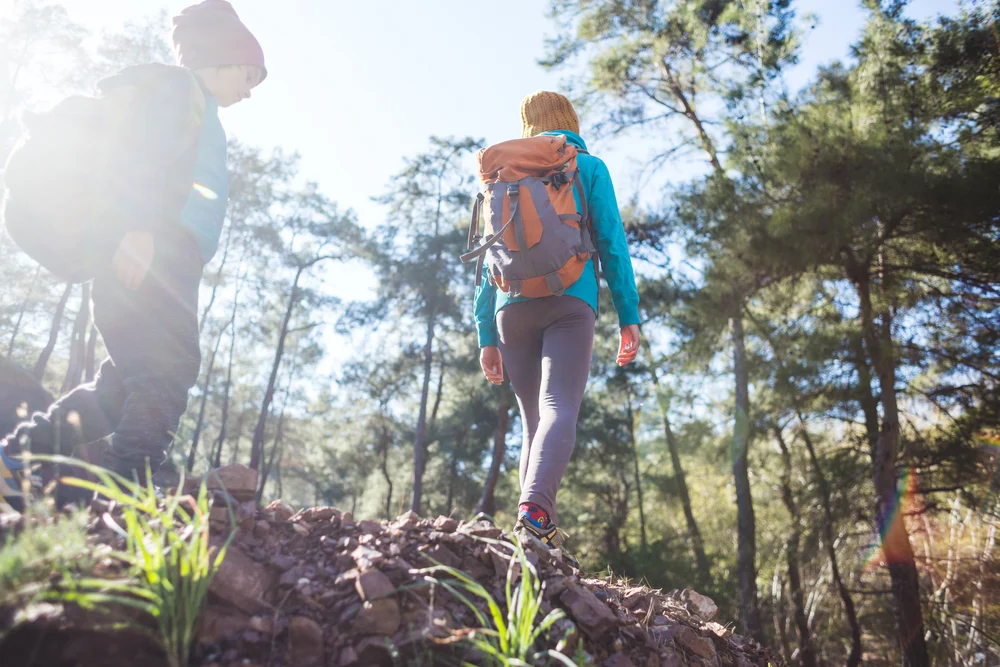 Woman and man wearing patagonia clothing whilst hiking up a woody hill