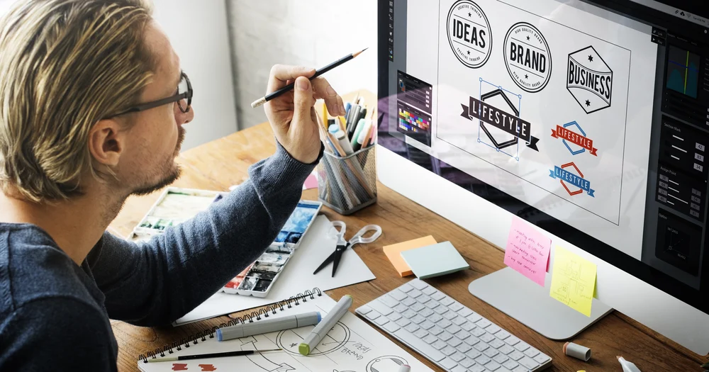 A graphic designer working on their Mac computer, designing multiple logos to grasp an understanding of what is corporate branding.