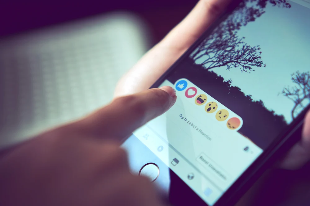 The Facebook app on an iPhone with a person liking a post to show how Facebook has impacted business marketing over the years.
