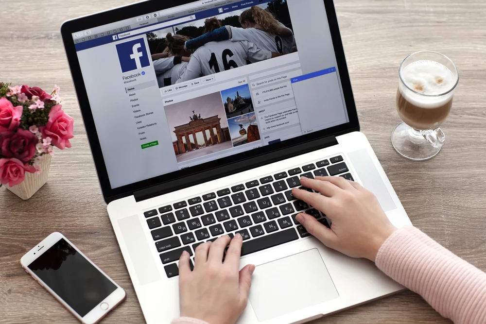 The Facebook website with a social media marketer logging in on their MacBook with a latte in clear glass.