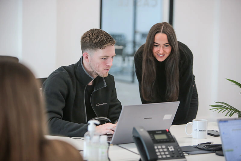 Castle Int. colleagues reviewing a project on a laptop at a desk in the Liverpool office
