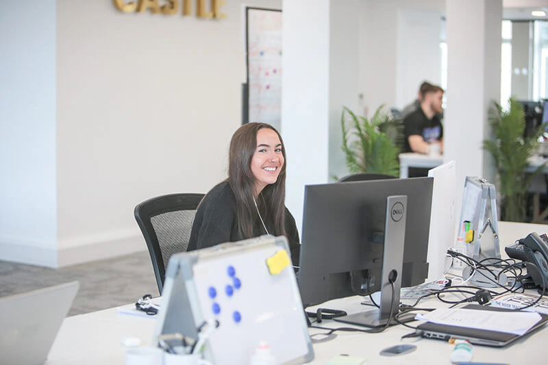 Castle Int. consultant smiling at her desk beneath the gold Castle Int. sign in the Liverpool office