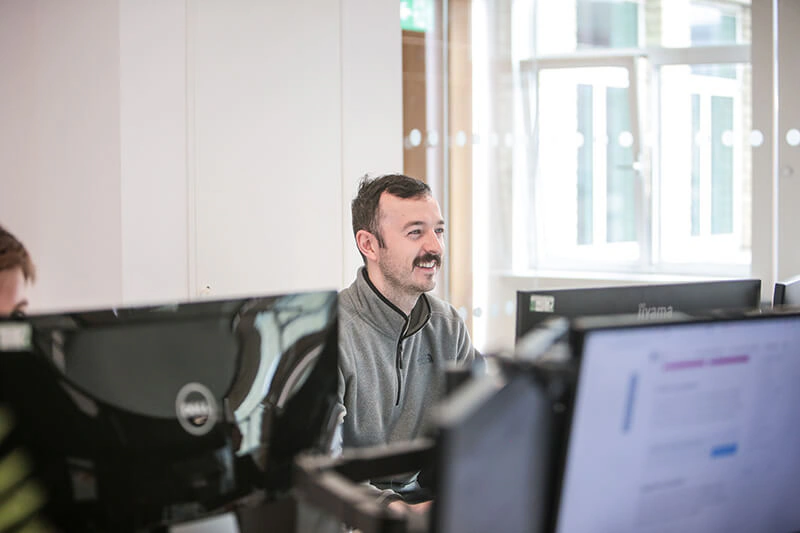 Castle Int. consultant smiling between monitors in the Liverpool office