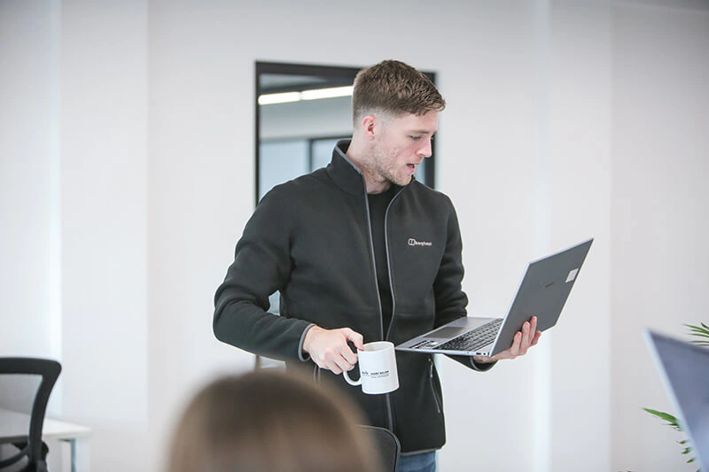 Castle Int. consultant standing with a laptop and mug of coffee in the office