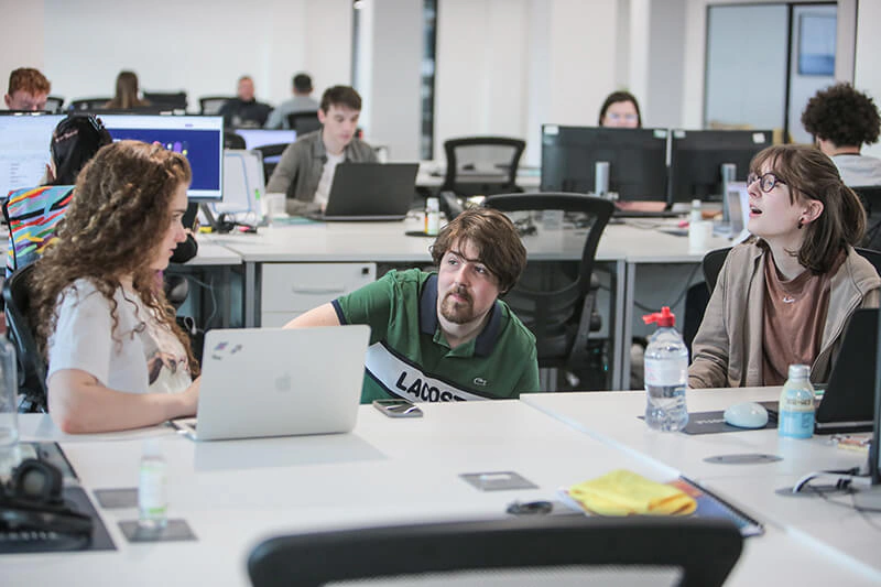 Castle Int. consultants chatting around a laptop in the busy open-plan Liverpool office