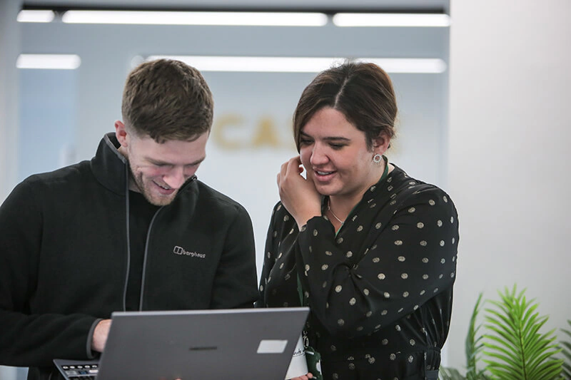 Two Castle Int. consultants smiling over a laptop in the agency's Liverpool office