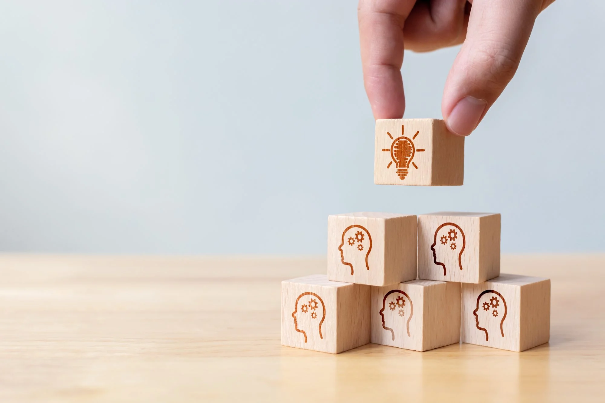 Hand placing a lightbulb block on a stack of wooden blocks printed with heads and cogs