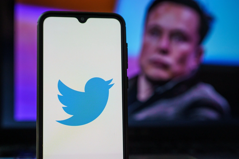 Twitter logo on a smartphone with Elon Musk pictured on a screen behind