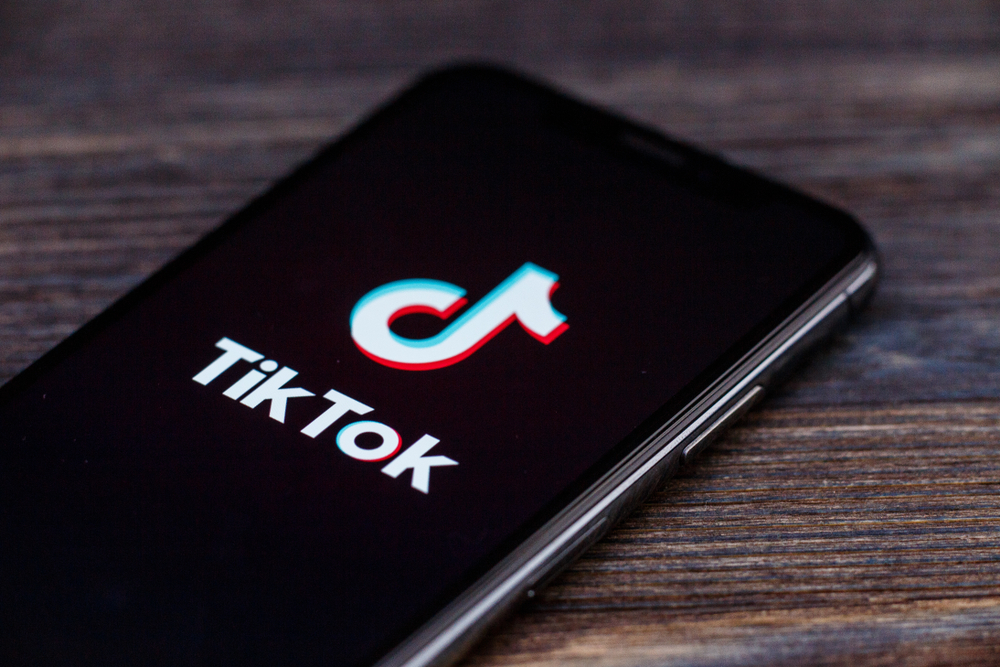 A smartphone displaying the TikTok logo on a wooden background.
