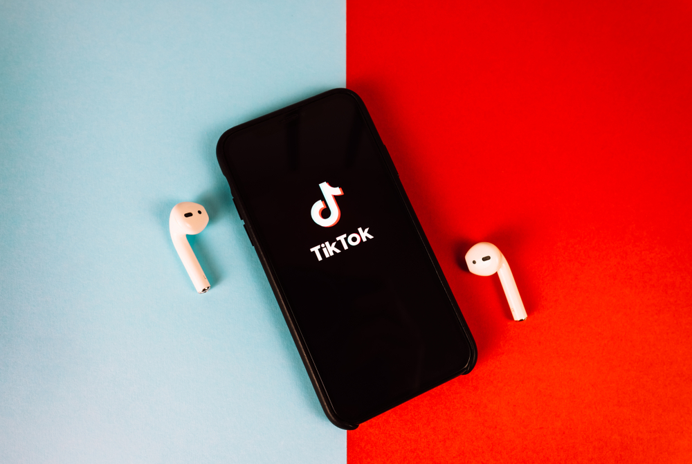 A phone displaying the TikTok logo with two white earphones next to it, on a blue and red background.