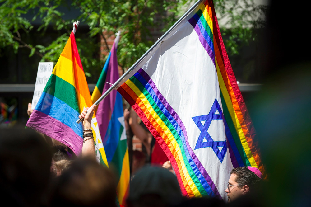 Rainbow Pride flags, one bearing a Star of David, held aloft at an outdoor march