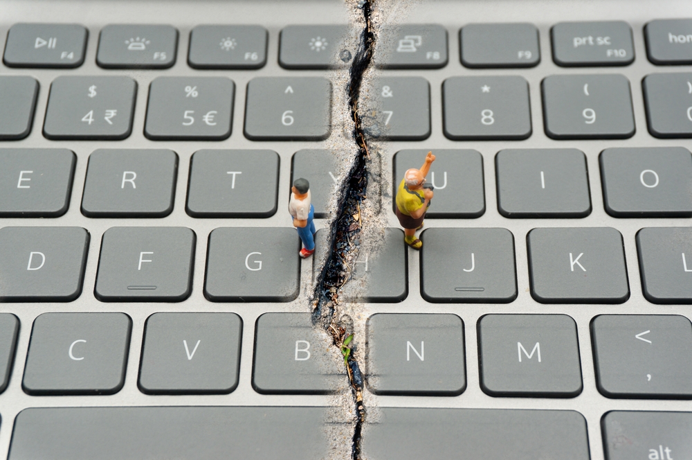 A keyboard divided by a large crack with a small figure standing on each side, facing away from each other.