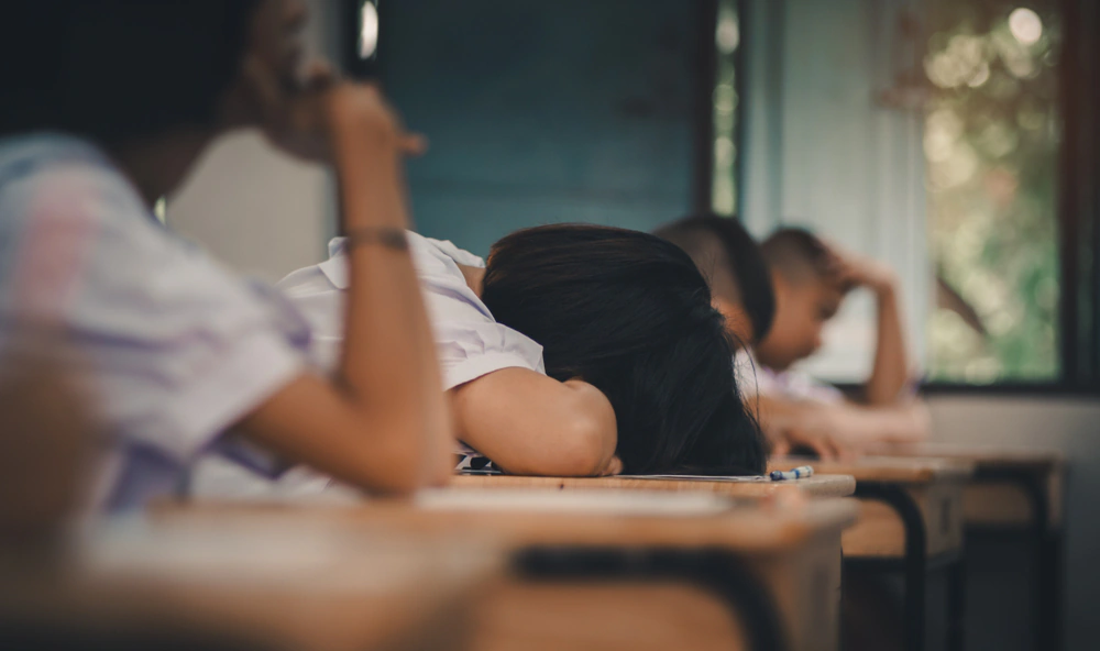Tired school pupils resting their heads on classroom desks