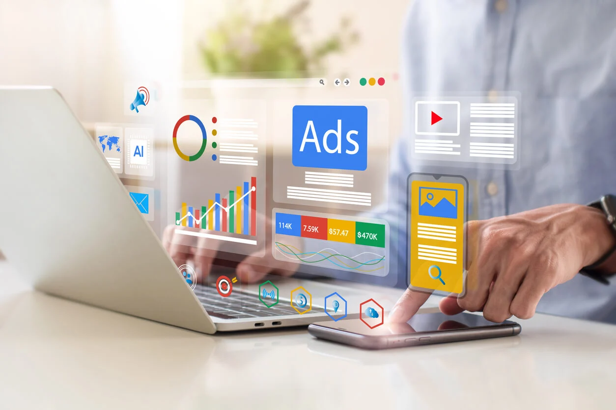 Image of a person sat at a desk using a laptop and a mobile phone. Hovering above the laptop and phone are graphics showing ads and stats