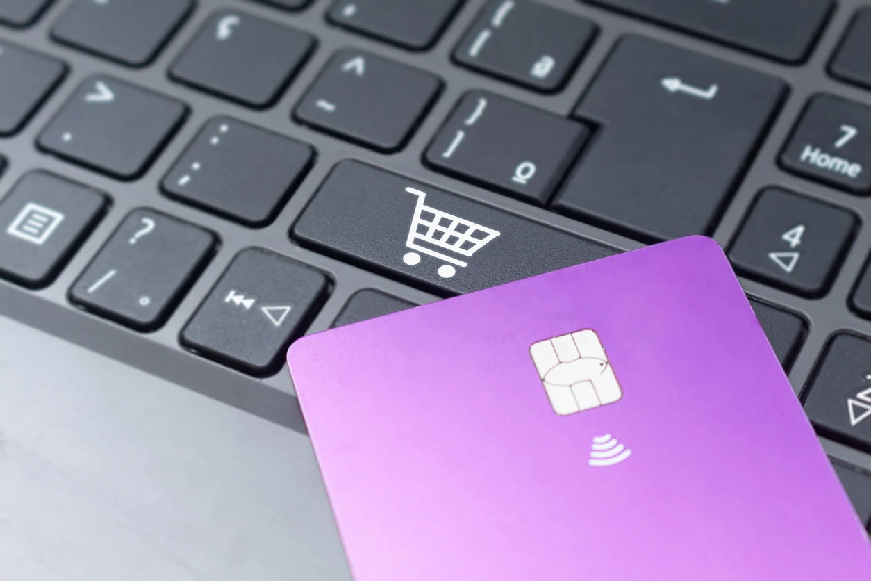 A picture of a purple credit card lying on top of a laptop keyboard with a shopping cart key in view.