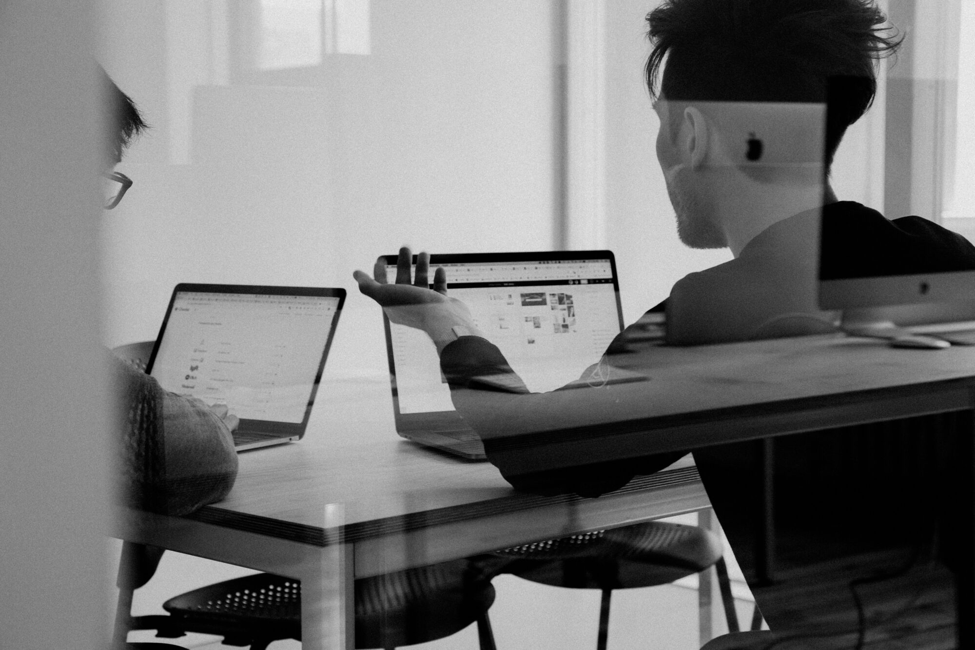 Two marketers discussing work across laptops in a black-and-white office meeting