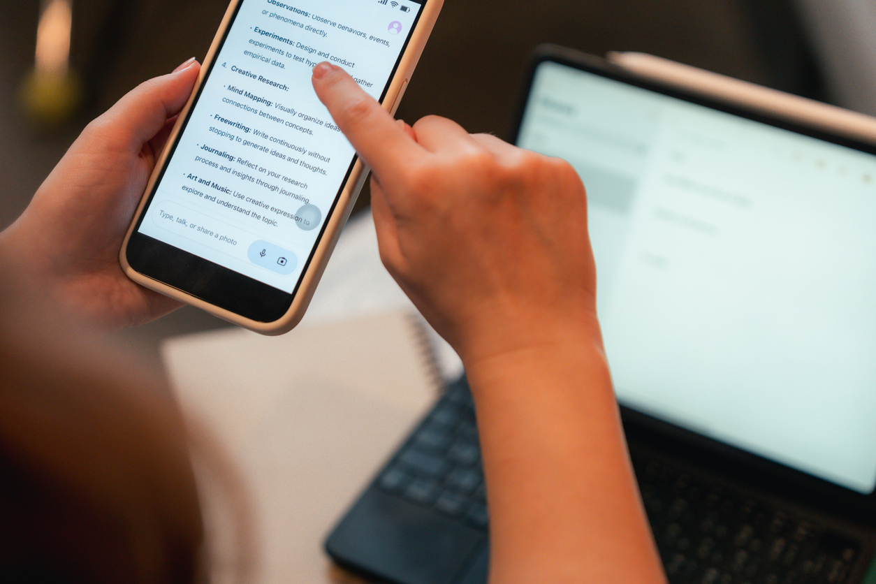 User interacting with an AI chatbot on a smartphone alongside a laptop, reviewing AI-generated information and productivity suggestions across multiple devices.